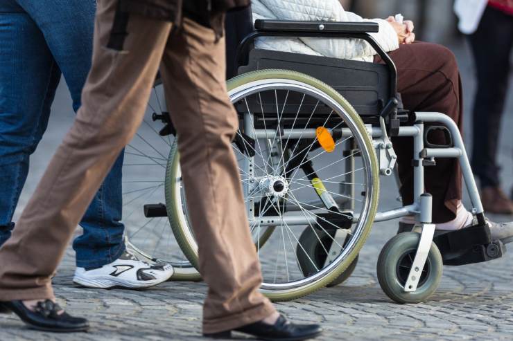 disabile su sedia a rotelle per strada con gente 