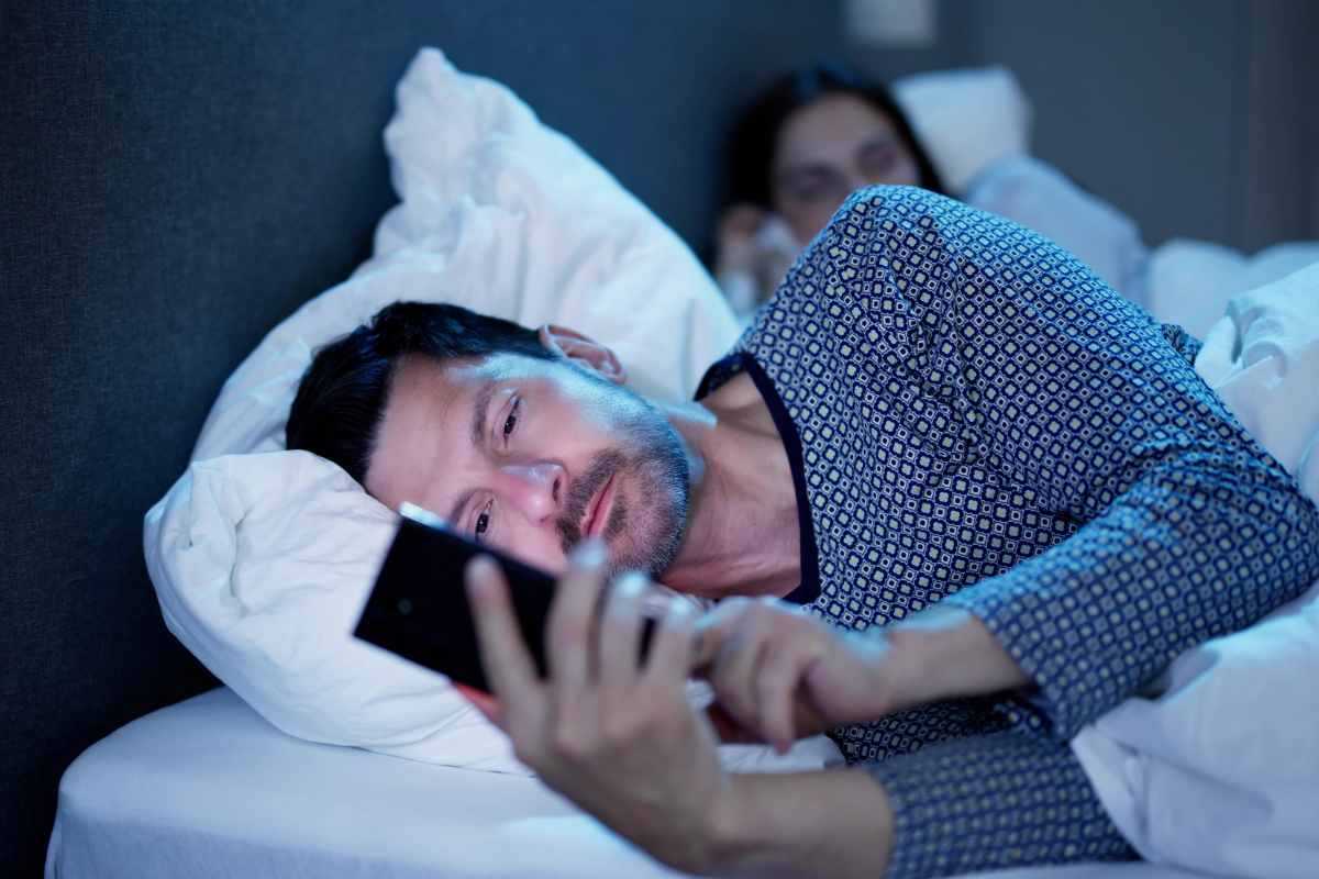 Uomo che guarda lo smartphone mentre è a letto con la compagna