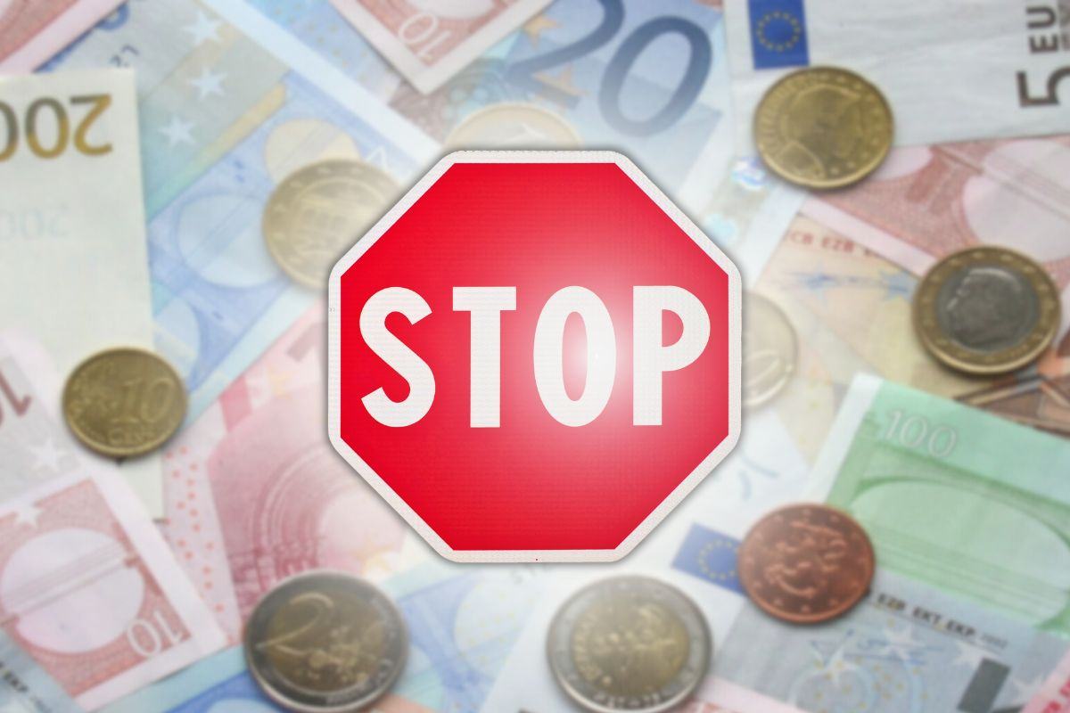 focus cartello stop per sospensione e sfondo con banconote e monete euro