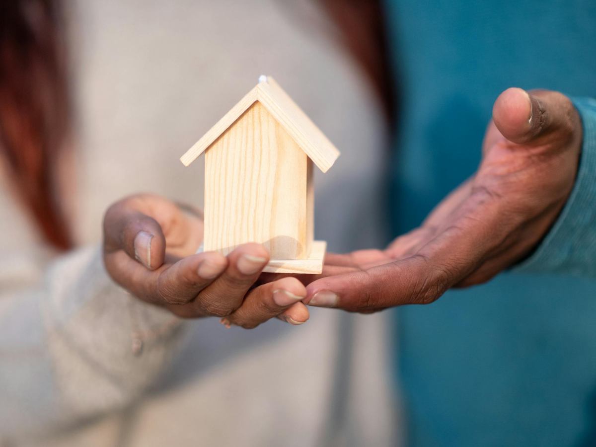 Persona che ha in mano la miniatura di una casa