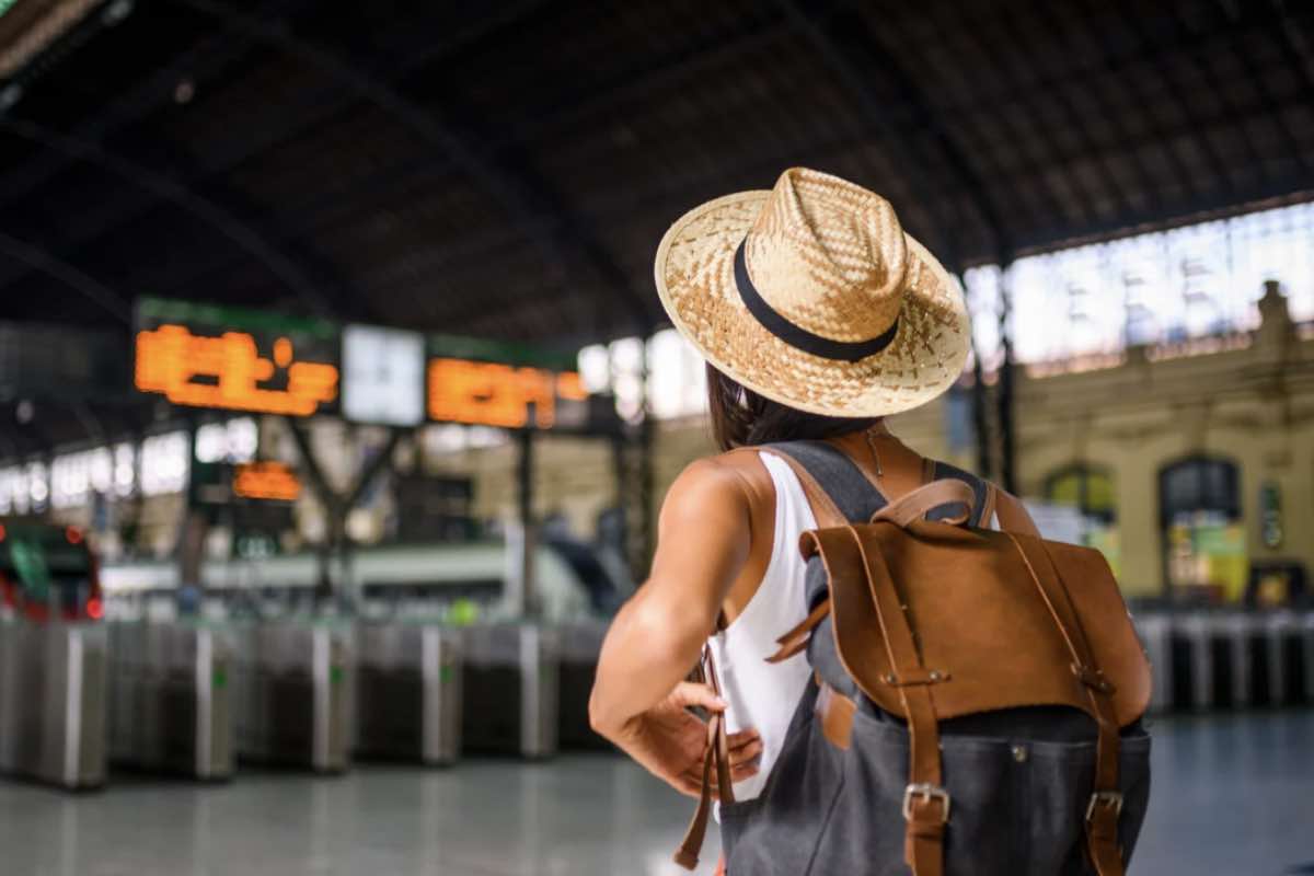 donna con zaino in spalla e cappello, che si dirige verso i treni per partire 