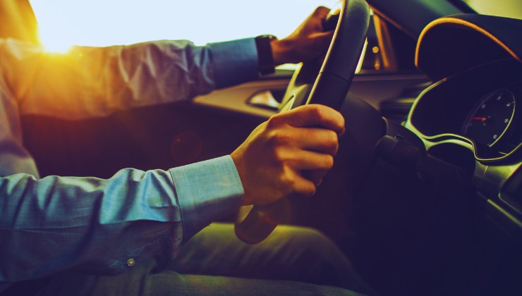 mani sul volante, uomo in camicia alla guida di un'auto