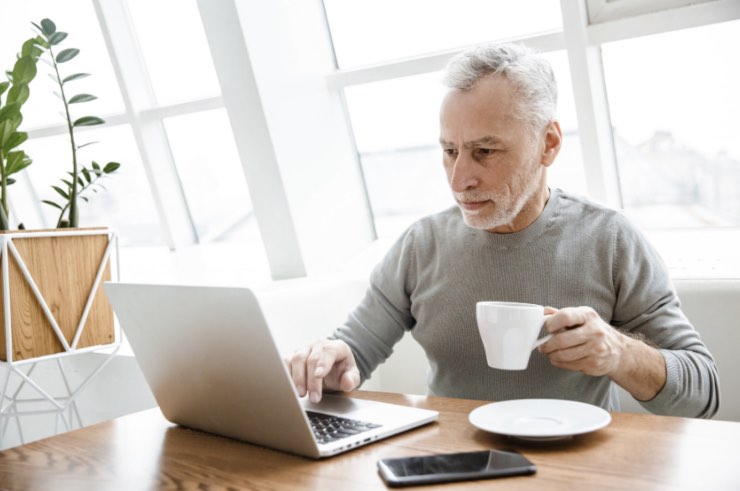 Signore di mezza età lavora al computer con tazza di caffè in mano