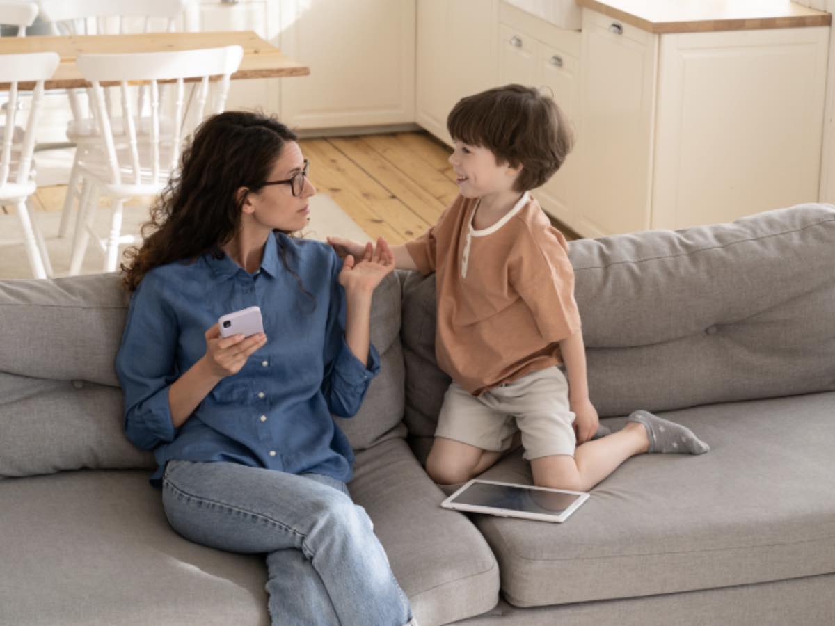 Mamma con lo smartphone parla con il figlio piccolo sul divano