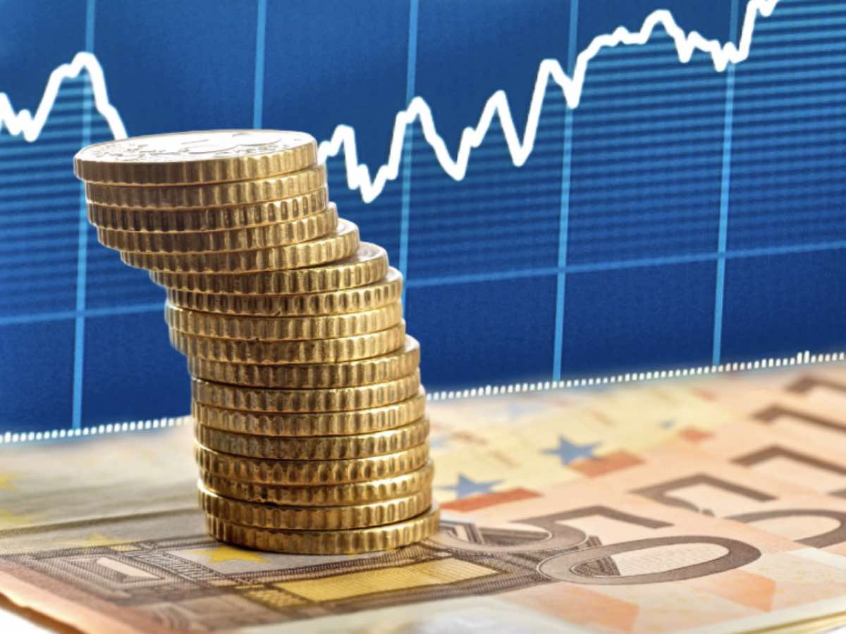 Pila di monete e banconote in euro, sullo sfondo un grafico finanziario