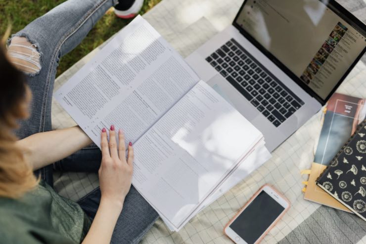 Ragazza che studia davanti al computer con un libro in mano