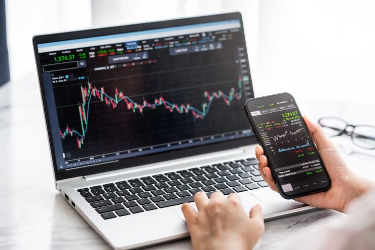 ragazzo fa analisi trading con pc e smartphone 