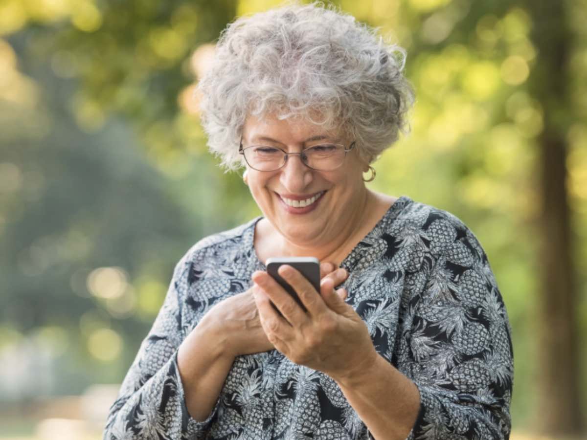 Signora anziana sorride mentre guarda lo smartphone