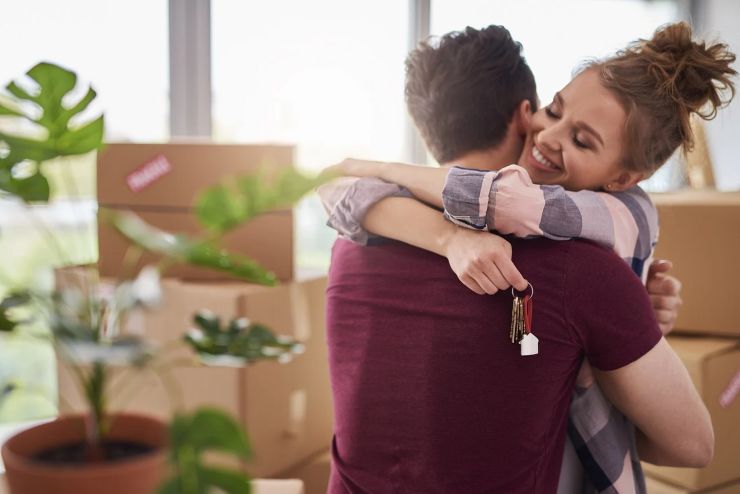 coppia si abbraccia dentro casa nuova, sullo sfondo scatoloni